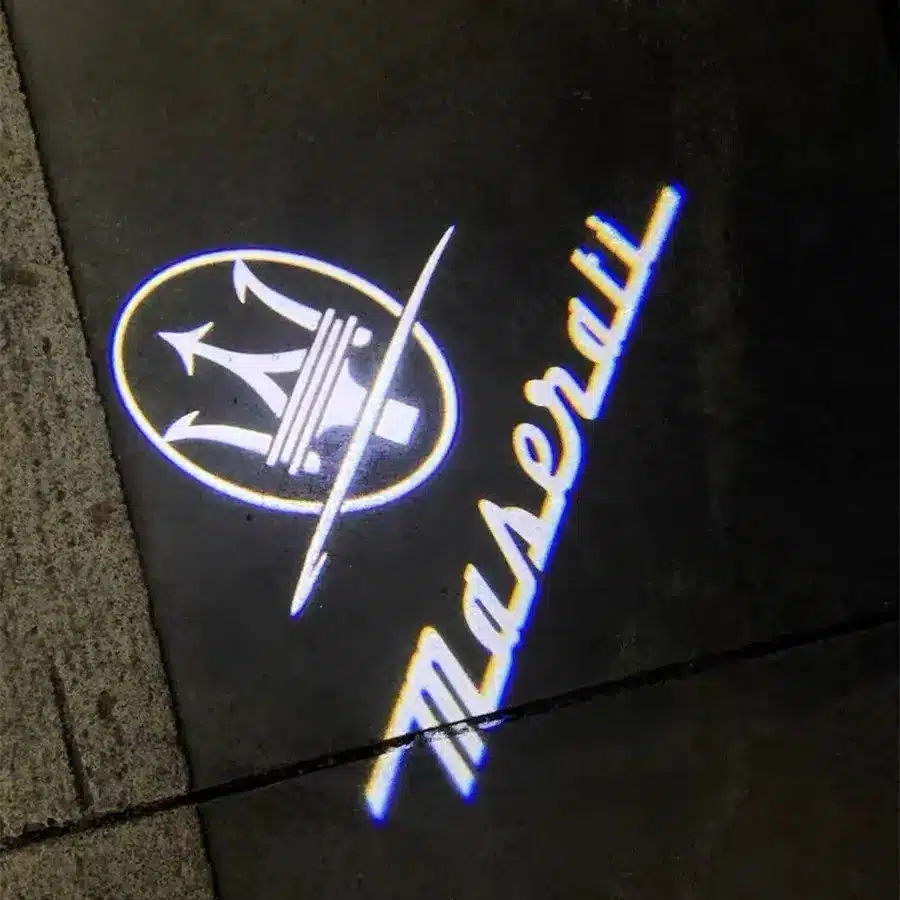 Nighttime illumination of Maserati door ghost lights showing the glowing blue and white emblem on the pavement.